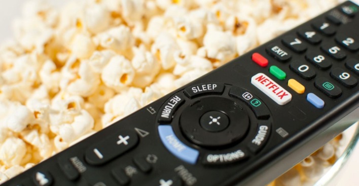 schwarze Fernbedienung mit weißem Netflix-Knopf mit roter Aufschrift "Netflix", liegt auf Popcorn