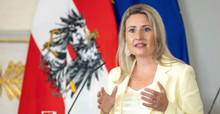 Susanne Raab spricht bei einer Pressekonferenz, im Hintergrund die österreichische und die EU-Flagge.