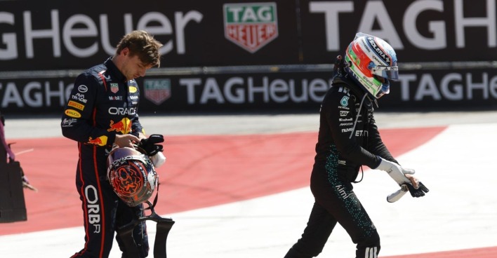 Red-Bull-Fahrer Verstappen hält seinen Helm und blickt frustriert zu Boden, während Mercedes-Pilot Antonelli mit Helm und Handschuhen davonläuft – Szene nach einem Unfall auf einer Formel-1-Strecke.