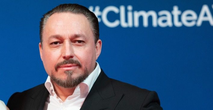 Porträt von Klemens Hallmann vor blauem Hintergrund mit „#ClimateAction“-Schriftzug, im dunklen Anzug und weißem Hemd.
