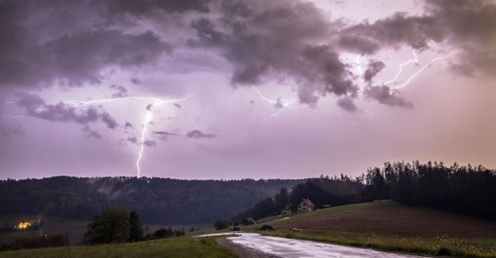 Unwetter in Österreich: dunkler Himmel mit Blitzeinschlag über einem Wald