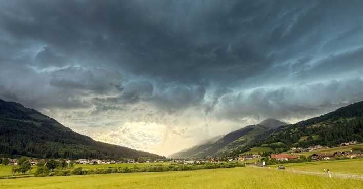 Dunkle Gewitterwolken über einem alpinen Tal, im Vordergrund grüne Wiesen und ein kleines Dorf; Unwetterfront im Anmarsch.: Katastrophale Unwetter zogen in den Abendstunden am Alpenrand entlang. Besonders heftig betroffen war der Landkreis Garmisch-Partenkirchen und Tirol. Am Achensee kurz vor der deutschen Grenze fiel Golfballhagel.