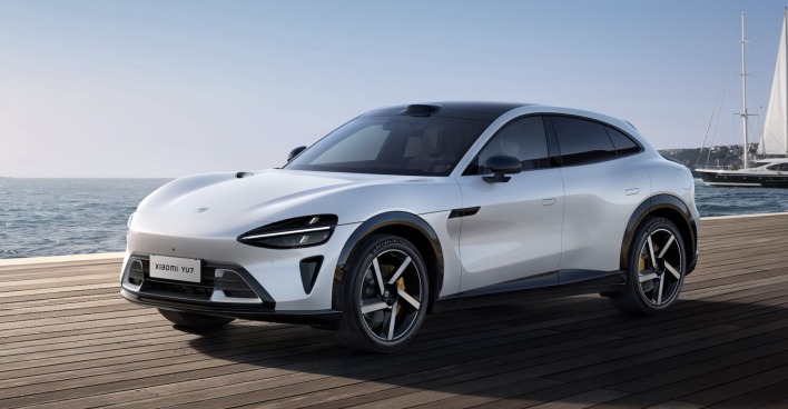 Der weiße Xiaomi YU7 Elektro-SUV steht auf einem Holzsteg vor dem Meer, im Hintergrund ein Segelboot – sportlich-elegantes Fahrzeug mit aerodynamischer Linienführung.