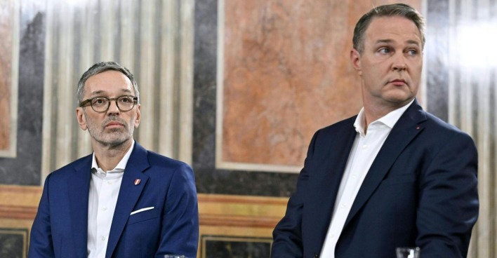 Herbert Kickl und Andreas Babler sitzen nebeneinander in einem prunkvollen Saal, beide in dunklen Anzügen, mit ernsten Mienen und Blicken in entgegengesetzte Richtungen.