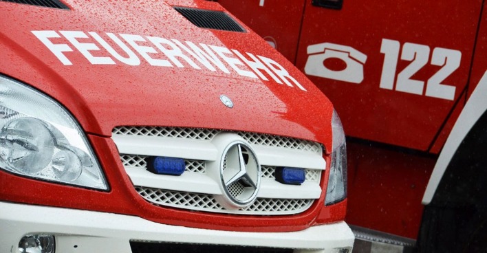 Nahaufnahme eines roten Feuerwehrfahrzeugs mit der Aufschrift „FEUERWEHR“ und dem Notrufsymbol „122“, Regentropfen auf der Motorhaube.