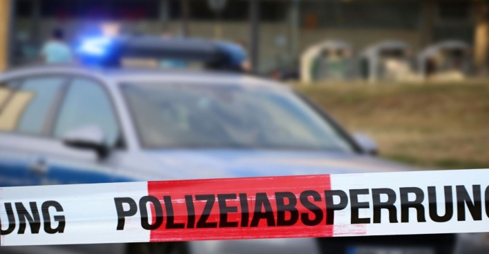 Polizeiwagen an einem Tatort, davor ist ein Polizeiabsperrband befestigt