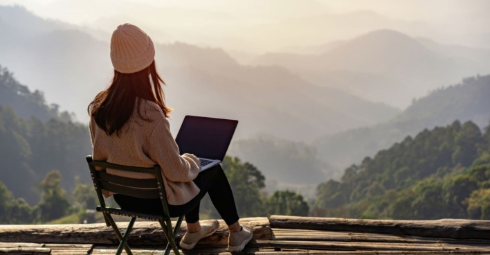 Frau arbeitet auf ihrem Laptop vor einer Bergkulisse