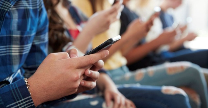Jugendliche sitzend, mit Smartphone in der Hand