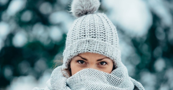 Junge Frau in Winterbekleidung steht vor verschneiten Bäumen