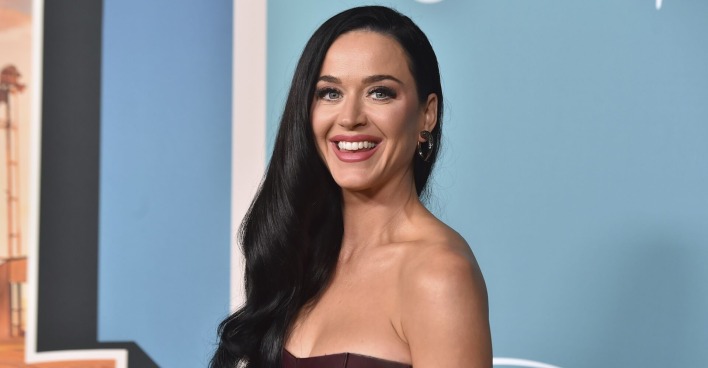 Katy Perry mit offenen, schwarzen Haaren vor blauem Hintergrund