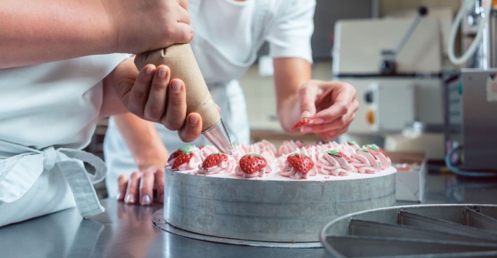 Konditoren mit Spritzbeutel in der Hand beim Verzieren einer Erdbeertorte
