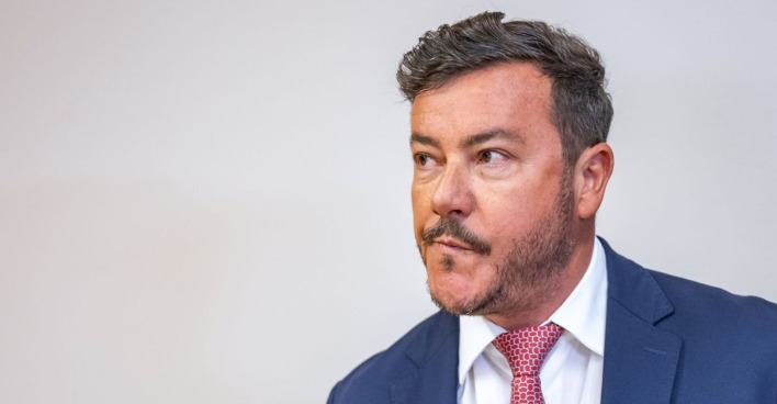 René Benko, im blauen Anzug mit roter Krawatte, verzieht das Gesicht und schaut zur Seite