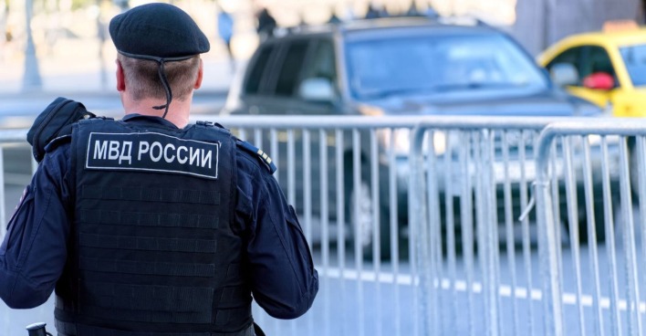 Russischer Polizist der Nationalgarde in kugelsicherer Weste patrouilliert durch die Straßen der Stadt, vor ihm ist ein Zaun, dahinter ein Auto
