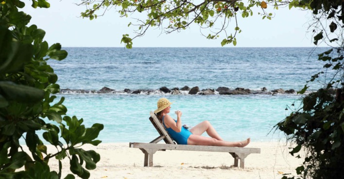 Frau im Badeanzug und mit Sonnenhut liegt auf einer Liege am Strand