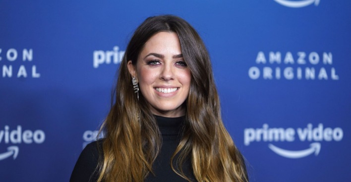 Vanessa Mai bei einer Amazon Prime-Premiere, schwarz gekleidet mit silbernen Ohrringen vor blauem Hintergrundit