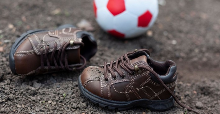 Kinderschuhe auf matschigem Boden, im Hintergrund liegt ein Fußball