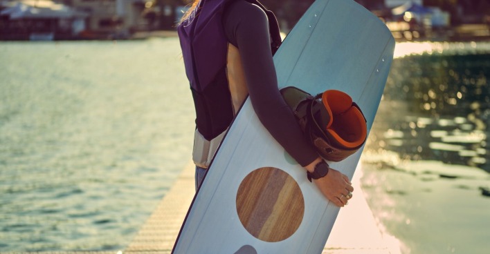 Ein Mädchen hält an einem See ein Wakeboard in der Hand.