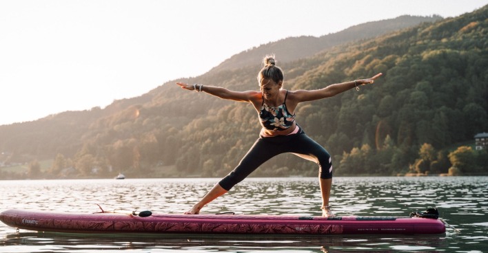 Eine Frau macht Yoga auf einem SUP auf dem Wasser.