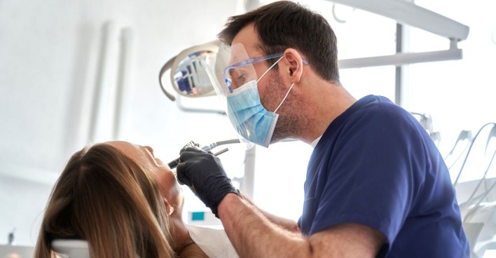 Zahnarztpraxis mit Arzt in blauer Kleidung und Patientin, die behandelt wird
