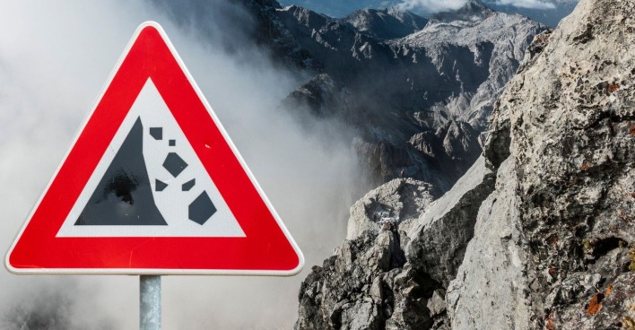 Fotoaufnahme der bayrischen Alpen im nebel, neben einem Warnschild vor Felsstürzen