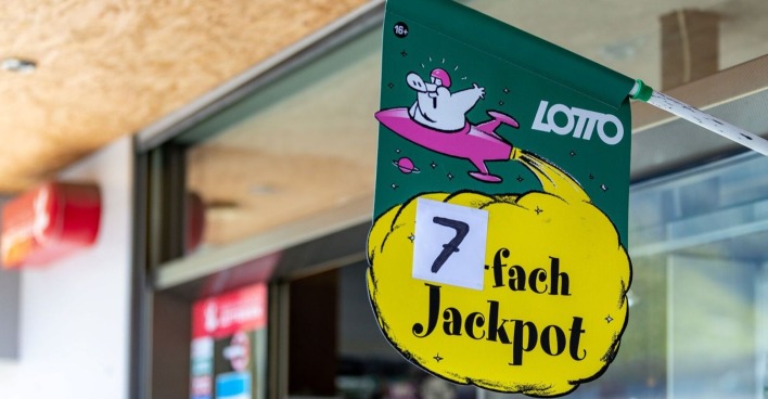 Grünes Lotto-Plakat mit gelber Wolke und der Aufschrift „7-fach Jackpot“ vor einer Trafik in Österreich.