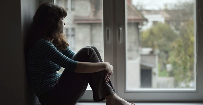 Frau sitzt traurig beim Fenster | Credit: iStock.com/Tunatura