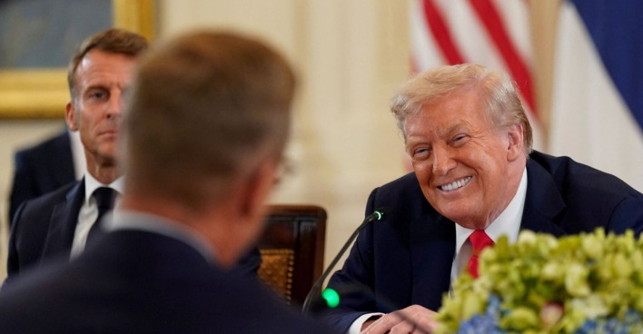 Donald Trump lächelt breit bei einem Treffen im Weißen Haus,  im Hintergrund Emmanuel Macron mit ernstem Blick.