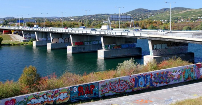 Blick auf eine Brücke über die Neue Donau in Wien, mit bunten Graffiti an den Brückenpfeilern und Mauern im Vordergrund. Im Wasser unterhalb der Brücke wurde eine Leiche gefunden.