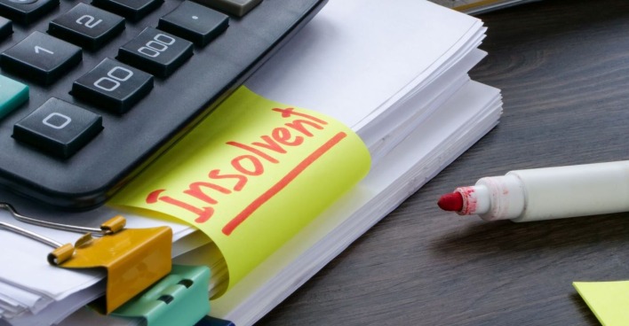 Bürotisch auf dem ein Stapel Papier mit einem Rotstift und ein Taschenrechner, auf einem Post-it steht das Wort insolvent geschrieben