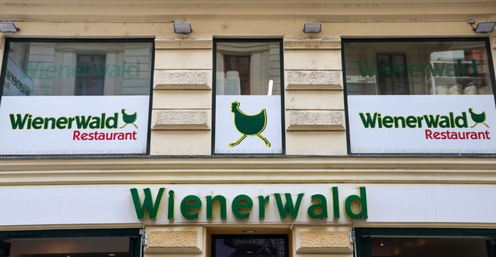 Logo des Wienerwald-Restaurants und Schild mit dem Symbol des laufenden Huhns an einer Gebäudefassade