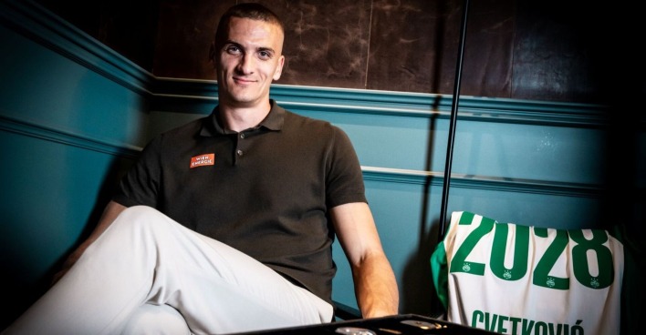 Nenad Cvetkovic in einem Poloshirt mit einem Sticker des Sponsors Wien Energie, im Hintergrund ein Rapid-Trikot, welches das jahr seines weiteren vertrages zeigt