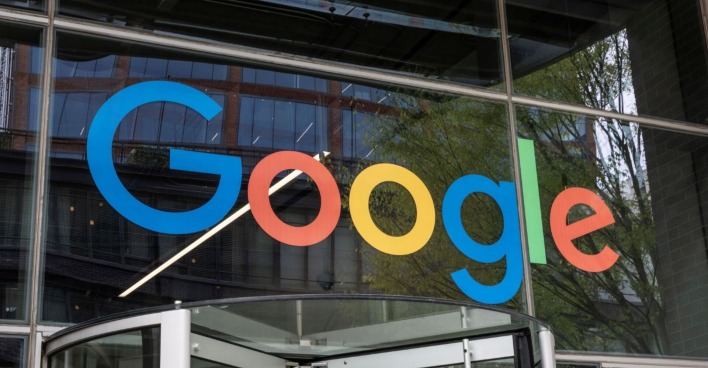 Großes, buntes Google-Logo an der Glasfassade eines Bürogebäudes, aufgenommen von außen mit Blick auf den Eingangsbereich.