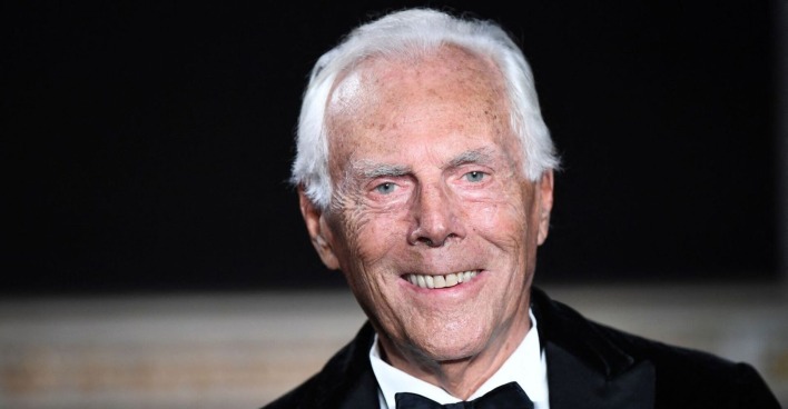 Porträt von Giorgio Armani mit weißem Haar, der im Smoking und mit Fliege in die Kamera lächelt.