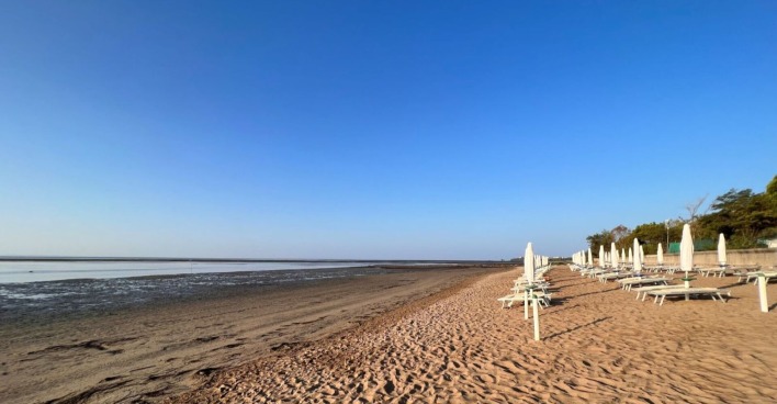 Leerer Sandstrand mit geschlossenen Sonnenschirmen und Liegen am Meer in Grado, Italien – Ort eines tödlichen Badeunfalls mit einem vierjährigen Kind.