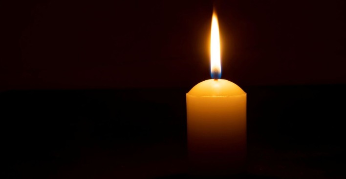 Einzelne brennende Kerzenflamme oder Licht, das auf einer großen weißen Kerze auf schwarzem oder dunklem Hintergrund auf dem Tisch in der Kirche für Weihnachten, Beerdigung oder Gedenkfeier mit Kopierraum leuchtet.