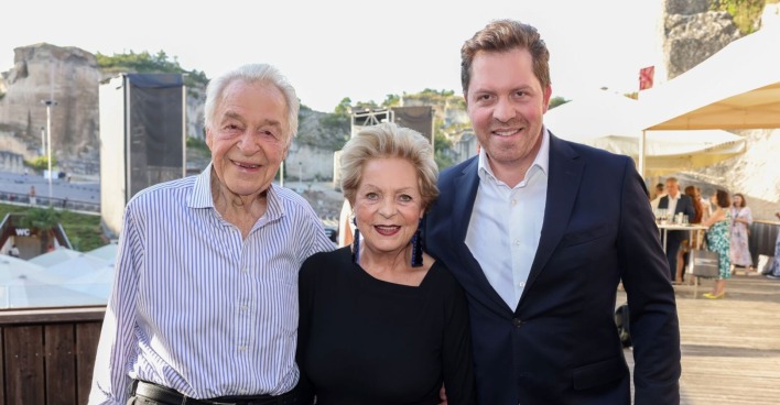 Harald Serafin steht lächelnd neben seiner Frau Ingeborg und Sohn Daniel. Im Hintergrund ist die Felsenbühne der Oper im Steinbruch St. Margarethen zu sehen.