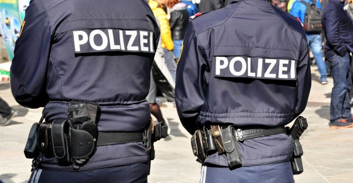 Zwei österreichische Polizisten in einer belebten Fußgängerzone stehend, an einem sonnigen Tag