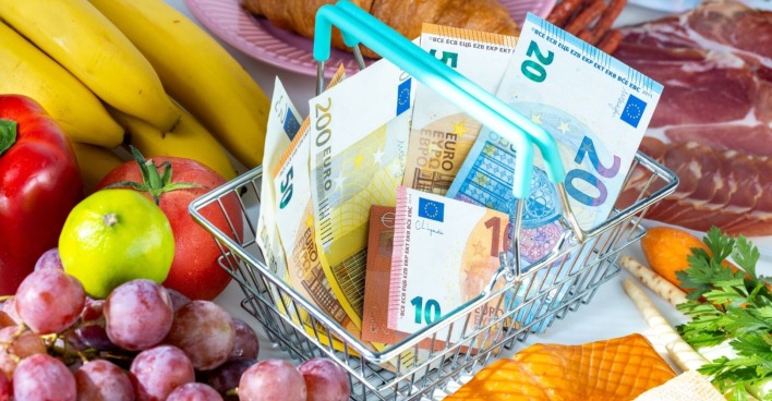 Einkaufskorb mit Euro-Banknoten zwischen Obst, Gemüse, Wurst und Käse – Symbolbild für steigende Lebensmittelpreise.