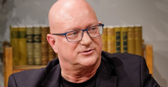 Porträt von Niki Glattauer mit Brille und schwarzem Sakko, aufgenommen während eines Gesprächs vor einem Bücherregal in der Sendung "Willkommen Österreich"