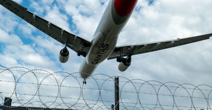 Flugzeug, welches über einem militärischen Sicherheitszaun abhebt