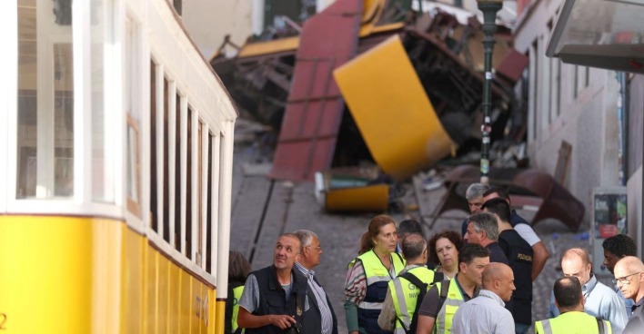 Ermittler und Einsatzkräfte stehen vor den Trümmern des entgleisten „Elevador da Glória“ in Lissabon – im Hintergrund der zerstörte gelbe Waggon.
