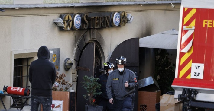 Polizisten mit Atemschutzmasken verlassen das ausgebrannte Lokal „Stern“ in der Grazer Sporgasse, davor beschädigte Einrichtung und ein Feuerlöscher.