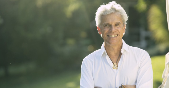 Thomas Brezina lächelt im weißen Hemd in die Kamera, Hintergrund Garten, Fokus auf seine Person.