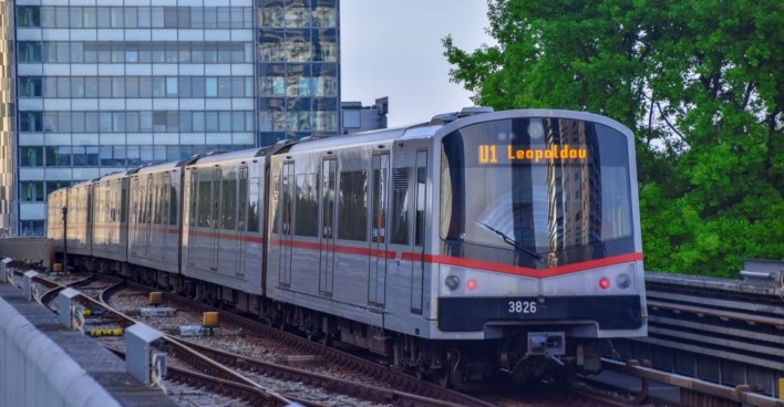 U-Bahn der Linie U1 in Wien auf oberirdischer Strecke, fährt in Richtung Leopoldau, umgeben von modernen Gebäuden und Bäumen.