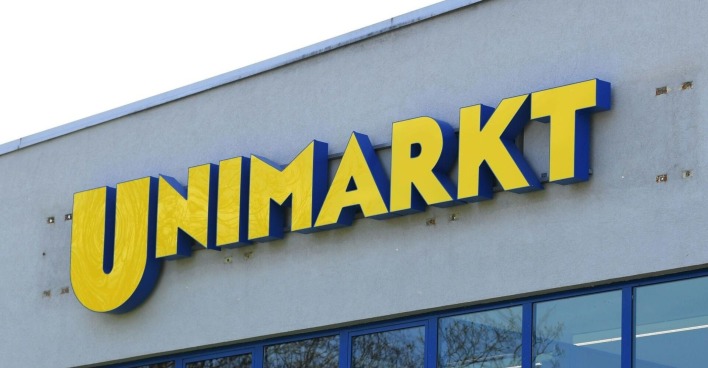 Gelbes Unimarkt-Logo auf grauer Fassade eines Supermarkts, Symbol für die angekündigte Schließung aller Filialen.
