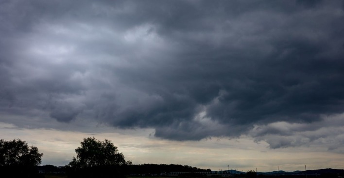 Dunkle, tiefhängende Gewitterwolken ziehen über eine Landschaft mit Bäumen und Hügeln im Hintergrund – Vorbote eines schweren Unwetters.