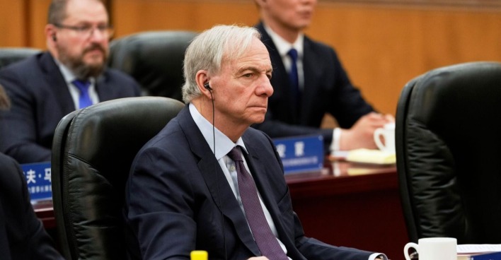 Ray Dalio sitzt im Anzug mit Kopfhörern bei einer Konferenz am Tisch, konzentrierter Gesichtsausdruck, weitere Teilnehmer im Hintergrund.