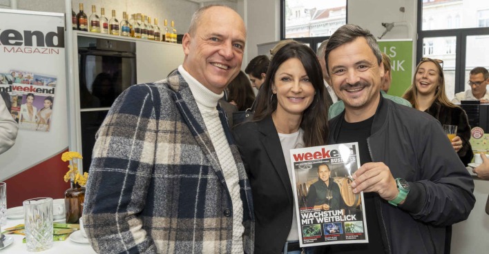 Eine Frau und zwei Männer lächeln und halten ein Magazin in die Kamera