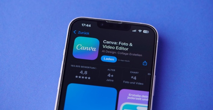 Ein Smartphone-Bildschirm zeigt das Canva-Logo auf einem iPhone im Apple-App-Store vor blauem Hintergrund