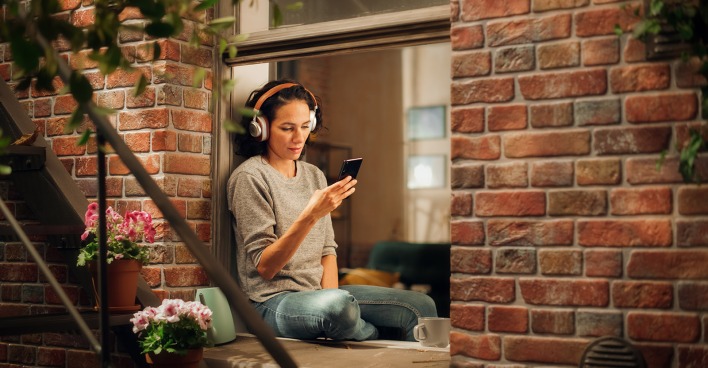 Frau sitzt am Fenster und hört einen Podcast | Credit: iStock.com/gorodenkoff
